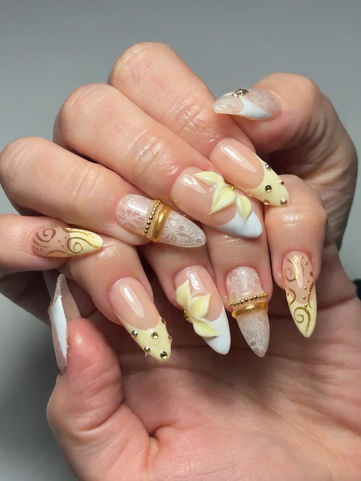Butter yellow almond Gel-X nails with 3D flowers, gold swirls and pearl charms